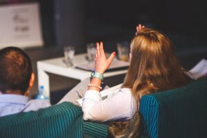 people in a business meeting watching something, with one woman holding her hands up 